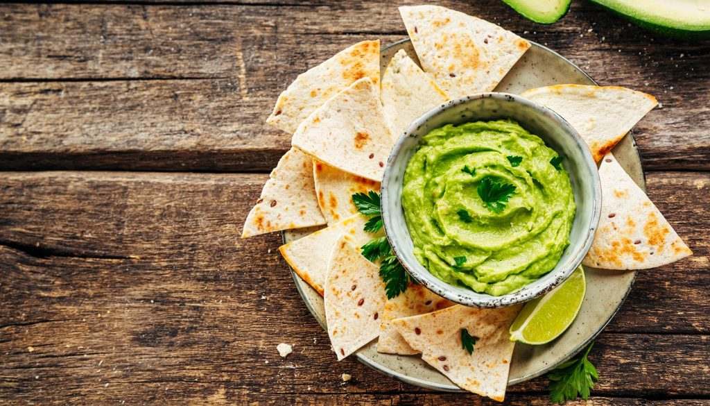 AvocadNachos on plate and avocado sauce, on rustic wooden board. The view from the top.ocreme