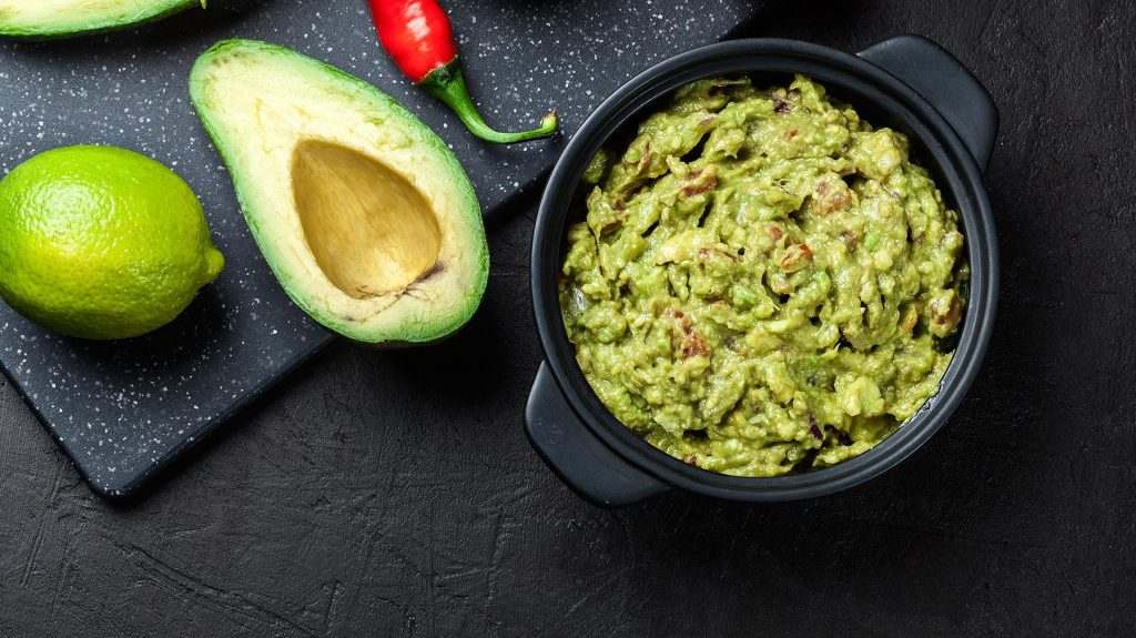 Bowl of guacamole with fresh ingredients on a black table