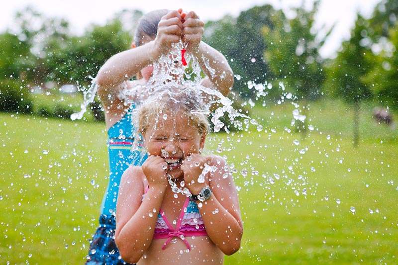 one girl splashing a water balloon to another girl