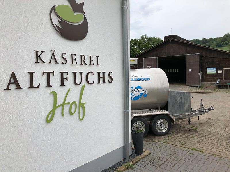 Käserei Altfuchshof Logo an Hauswand, im Hintergrund Bauernhof