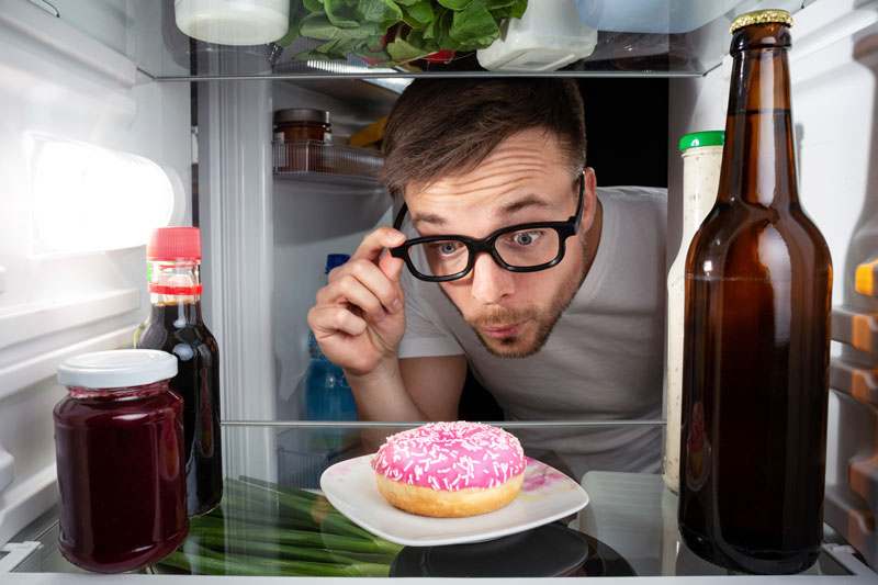 Mann entdeckt Donut im Kühlschrank und sieht ihn eindringlich an