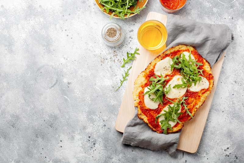 Pins auf grauem Betonhintergrund, belegt mit frischer Tomatensauce und Mozzarella-Scheiben